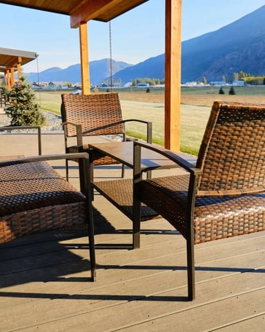 Wicker patio chairs on a covered deck overlooking open fields and mountains near Columbia Falls